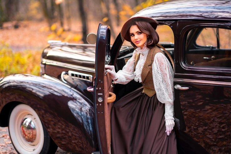 Photo beautiful female in vintage  dress, lace blouse and hat with veil standing near retro brown car