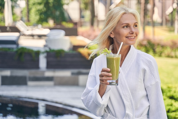 beautiful female with green smoothie in hand looking away while standing in the outdoors