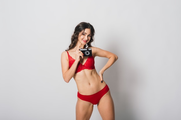 白で隔離、写真のカメラを保持している赤いランジェリー ピンナップ スタイルでかなり笑顔の美しい女性