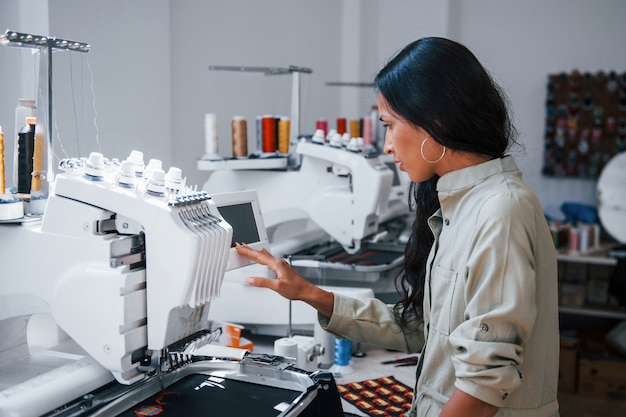 Beautiful female worker is in the sewing factory by the machine.