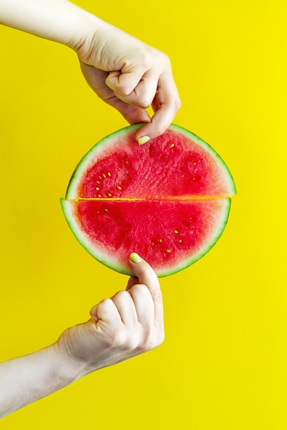 Beautiful feminine hands holding fresh tasty red appetizing watermelon slices on bright yellow background. Summer Family Relationship Friendship Concept.