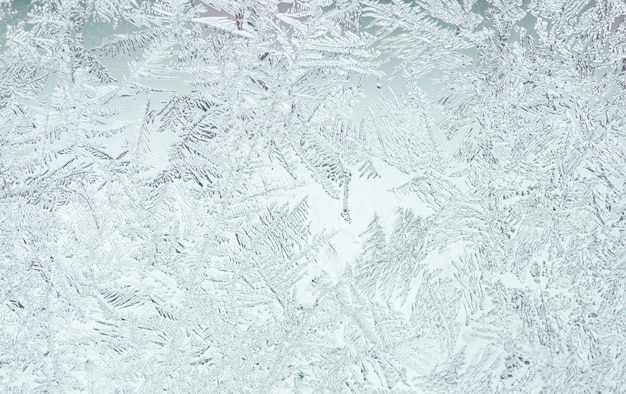 Photo beautiful festive frosty pattern with white snowflakes on a blue background on glass