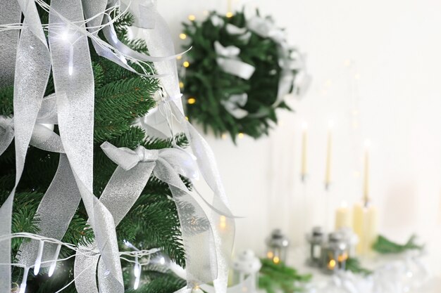 Beautiful fir tree with silver ribbons and Christmas lights in room closeup