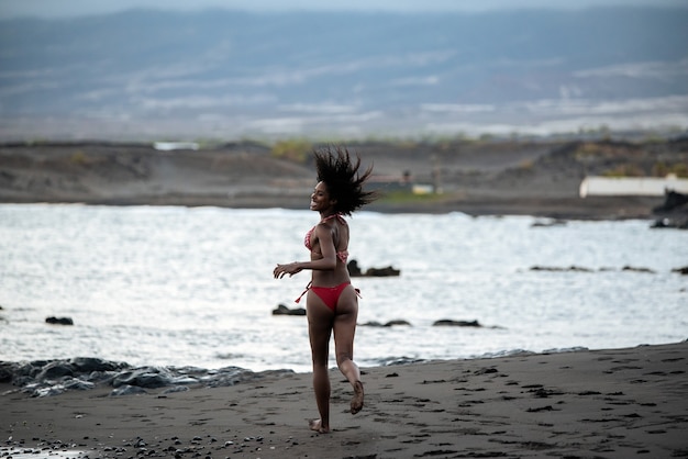 Beautiful fit playful black woman in bikini running in a volcanic beach in Santo Antao, Cape Verde