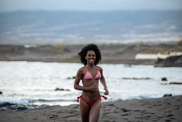 Bella vestibilità giocosa donna nera in bikini che corre su una spiaggia vulcanica a santo antao, capo verde