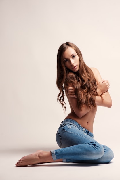 Bella donna topless sexy di misura in blue jeans che si trovano giù, isolato su fondo bianco