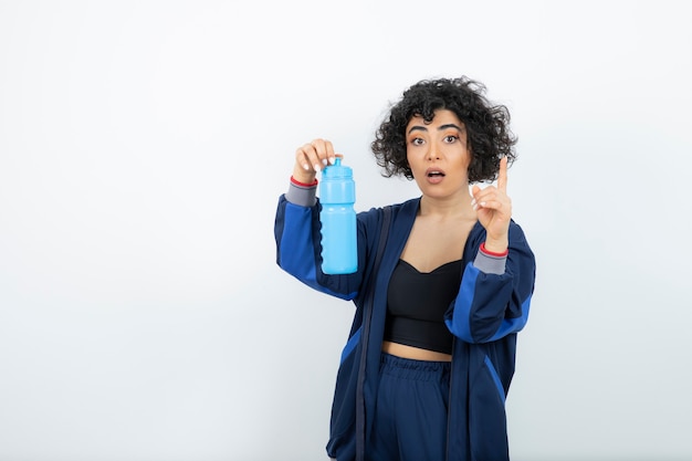 Красивейшая спортивная пригонка женщина держа бутылку голубой воды.