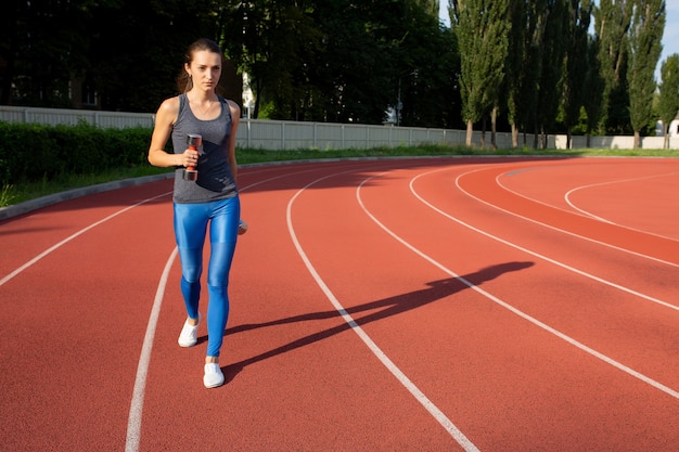 Beautiful fit woman doing excercises with dumbbells in the stadium in sunny day. Space for text