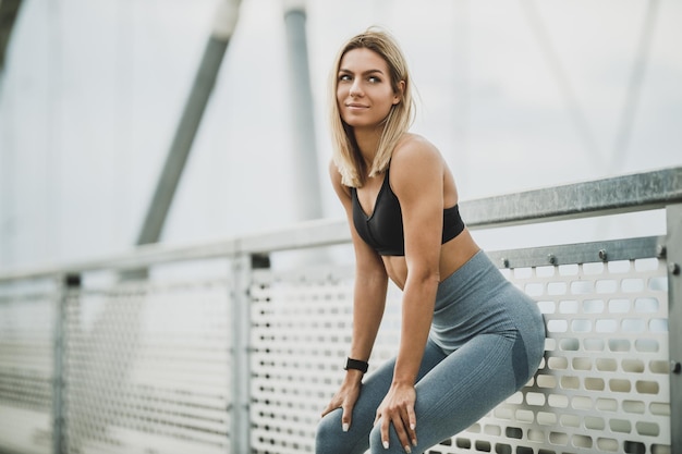 Beautiful fit woman standing and preparing for hard training on the bridge in the city.