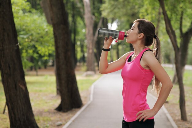 Красивая фитнес спортсменка бегун женщина питьевой воды в парке