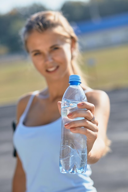 Beautiful fitness athlete woman drinking water after work out exercising on sunset evening summer in outdoor portrait