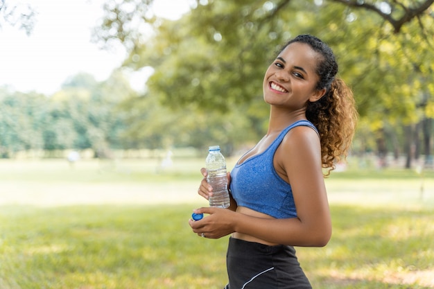 Beautiful fitness athlete woman drinking water for health after work out exercising in the park outdoor portrait