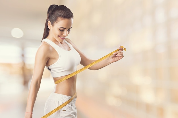 Beautiful fitness girl measuring her waistline with measure tape