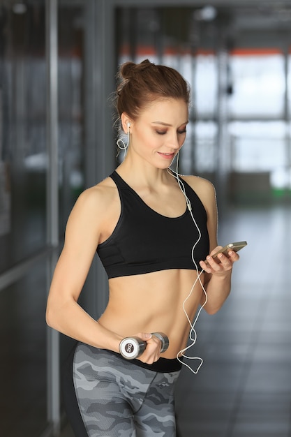 Beautiful fitness woman standing with dumbbells and looking at telephone