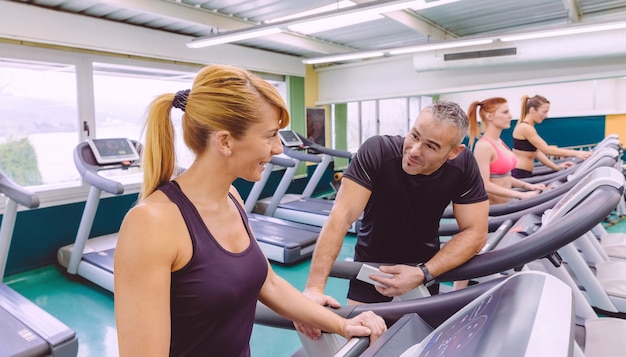 Beautiful fitness woman in a treadmill talking with handsome man on a fitness center