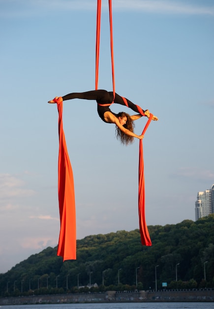 Beautiful flexible female artist with aerial silk on sky and river background