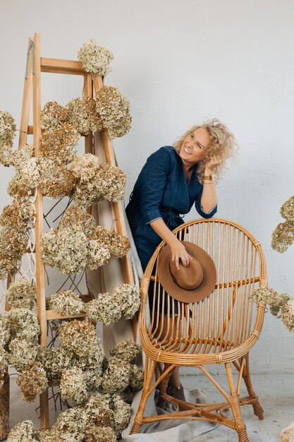 Beautiful floral arrangement including beautiful dried hydrangea flowers, in stylish space, on wooden staircase. Among them is happy smily woman florist in denim dress.