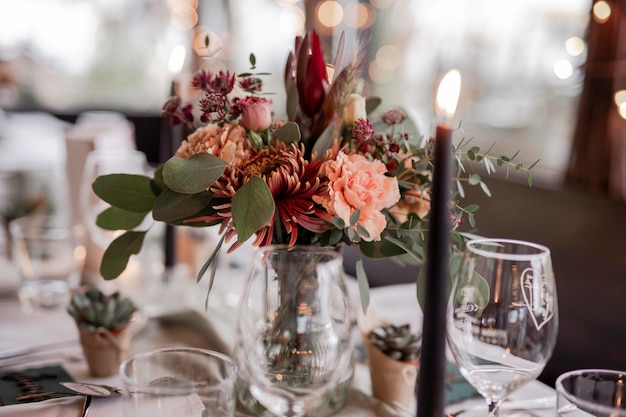 Beautiful flower bouquet burning candle and glasses on the wedding table