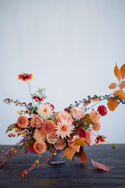 Beautiful flower composition with autumn orange and red flowers and berries Autumn bouquet in vintage vase on a white wall background