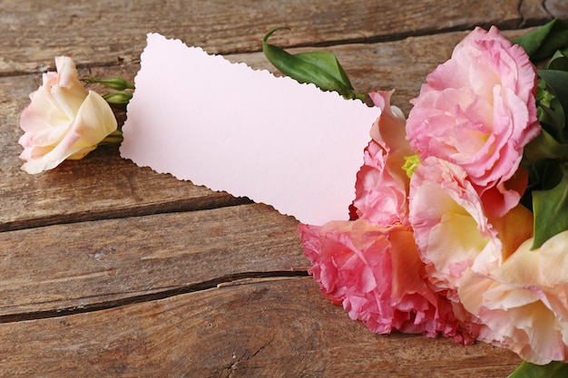 Beautiful flowers and gift card on wooden background