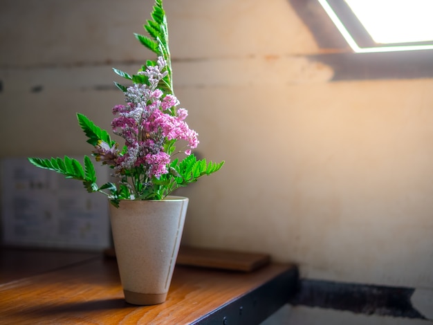 Foto bei fiori rosa e foglie verdi in un'annata bianca del vaso sulla tavola di legno accanto