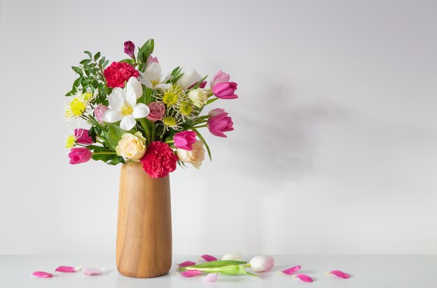 beautiful flowers in vase on shelf on background white wall