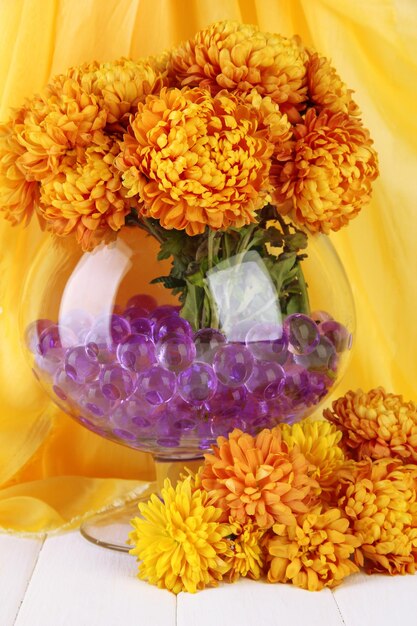 Beautiful flowers in vase with hydrogel on table on fabric background