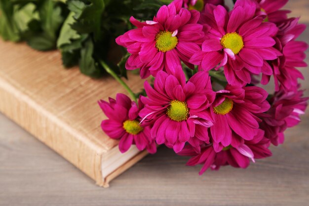 Beautiful flowers with book on wooden table closeup