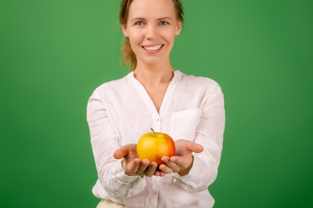 A beautiful fortyyearold woman holds a fresh apple in her hands on a green background Healthy eating vegetarianism healthy appearance concept