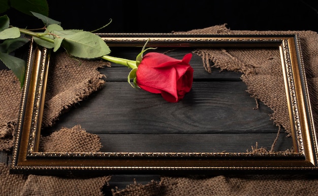 In a beautiful frame pieces of canvas and a red rose on a\
wooden background