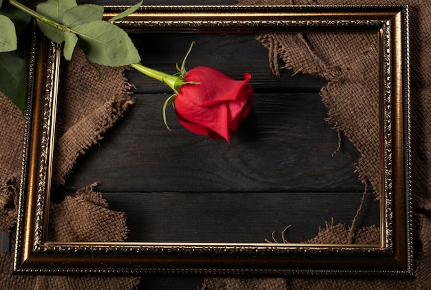 Photo in a beautiful frame pieces of canvas and a red rose on a wooden background