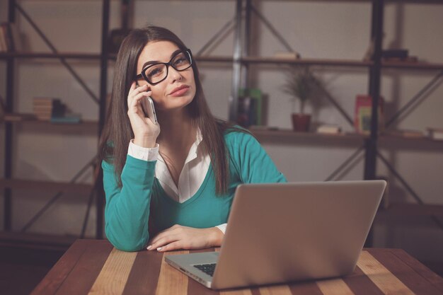 Beautiful freelancer is working with something and sitting at the wood table with laptop and phone