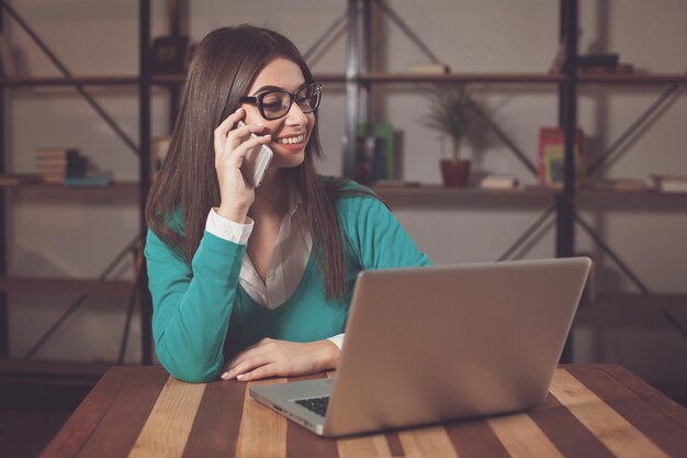 Beautiful freelancer is working with something and sitting at the wood table with laptop and phone