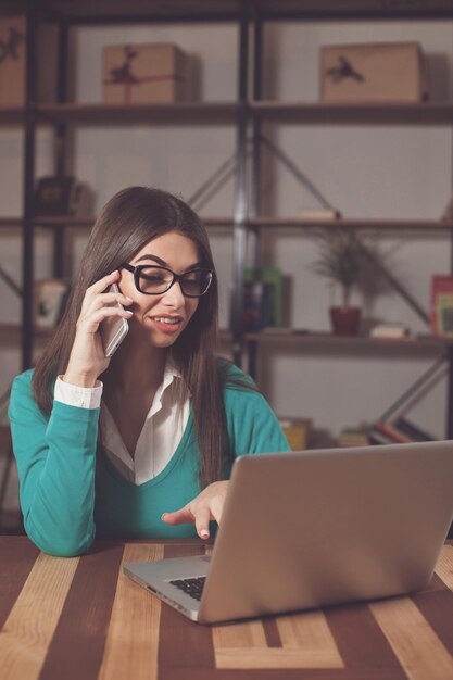 Beautiful freelancer is working with something and sitting at the wood table with laptop and phone