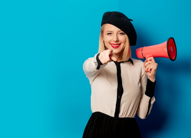 Beautiful french woman in beret holds  loud-hailer on blue wall