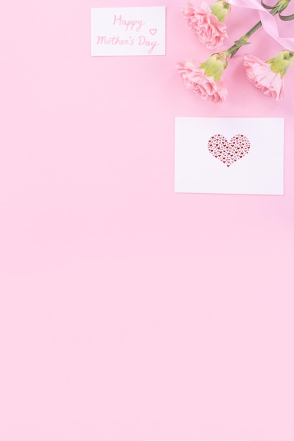 明るいピンク色の背景に分離された白い挨拶感謝ギフトカードと美しい新鮮でエレガントなカーネーションの花の花束トップビューフラットレイコンセプト