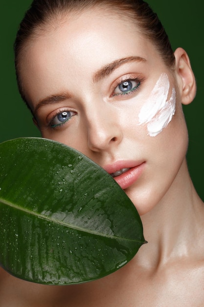 Beautiful fresh girl with cosmetic cream on the face natural makeup and green leaves Beauty face