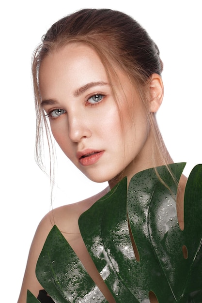 Beautiful fresh girl with perfect skin natural makeup and green leaves Beauty face Photo taken in the studio