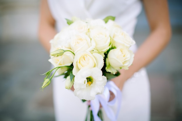 Beautiful fresh wedding bouquet of roses in beige light colors in the hands of the bride.