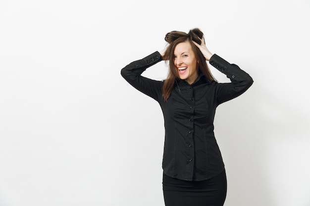 Beautiful fun caucasian young smiling brown-hair business woman in black classic shirt and skirt holding hair with hands isolated on white wall