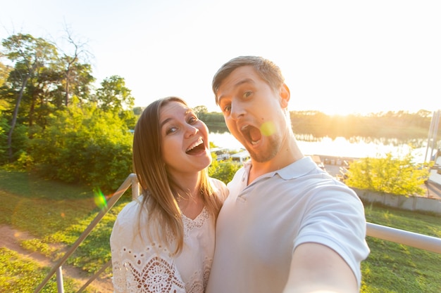 Beautiful funny romantic couple on nature background. Attractive young woman and handsome man are making selfie, smiling and looking at camera.