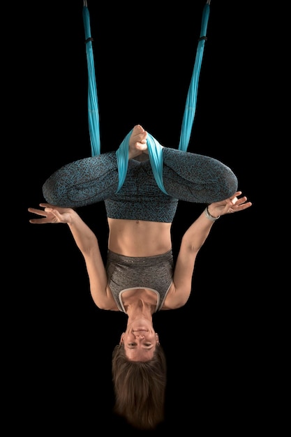 Beautiful funny young woman yoga instructor practicing fly yoga on black background Vertical frame Aerial antigravity yoga