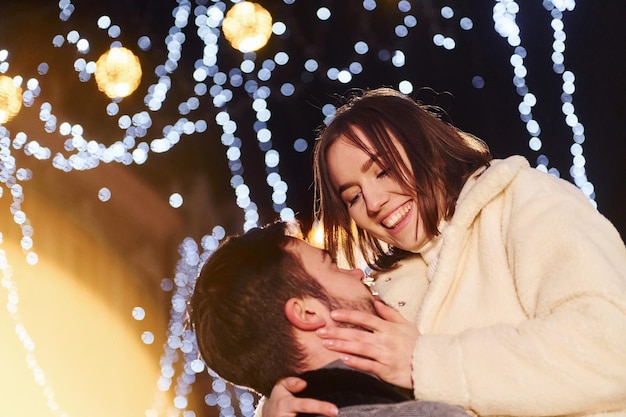 美しい花輪の照明通りで屋外で新年を祝う幸せな若いカップル