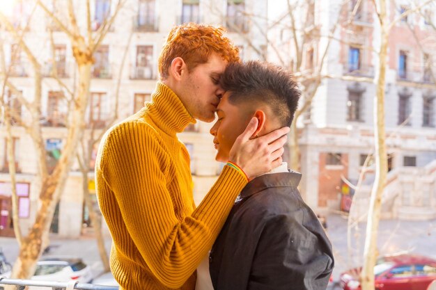 Beautiful gay couple being romantic at home on the sofa home balcony kissing each other on the forehead lgbt concept