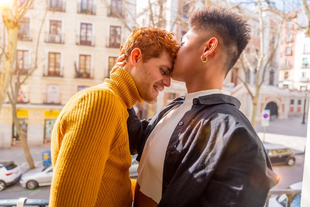 Beautiful gay couple being romantic at home on the sofa home balcony kissing each other on the forehead lgbt concept