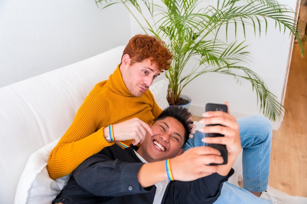 Beautiful gay couple being romantic indoors at home on the sofa gay couple taking selfie lgbt concept