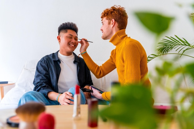 Beautiful gay couple putting on makeup and having fun being romantic indoors at home lgbt concept