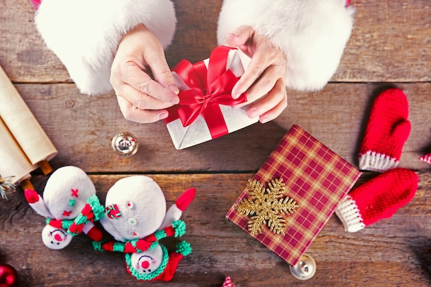 Beautiful gift box in Santa Claus's hands and Christmas decorations on wooden table, close up