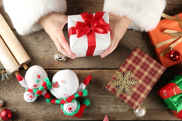 Bella confezione regalo nelle mani di babbo natale e decorazioni natalizie su un tavolo di legno, primo piano