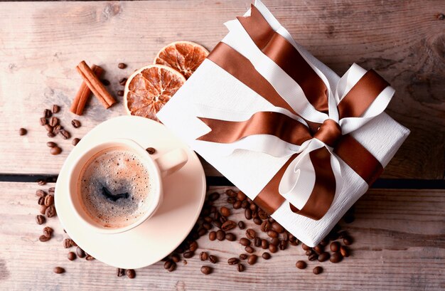 Красивый подарок, чашка с кофе и кофейные зерна на деревянном фоне